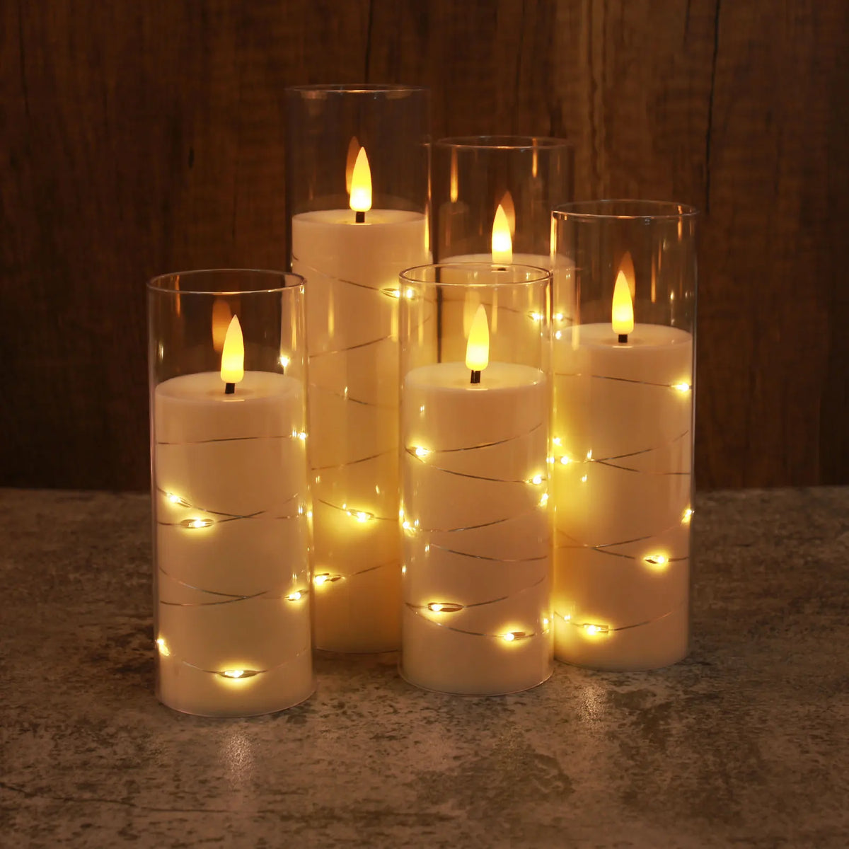 A set of glowing white candles in glass holders decorated with twinkling string lights and a visible flame.
