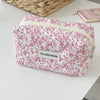 A pink floral quilted makeup bag with a zipper closure resting on a white surface.