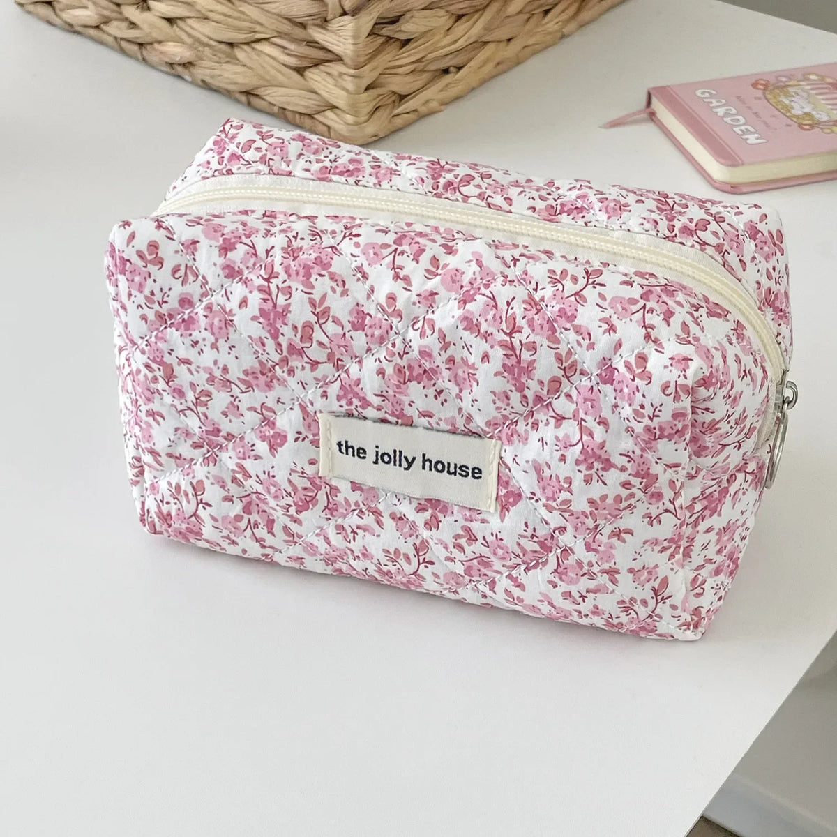 A pink floral quilted makeup bag with a zipper closure resting on a white surface.