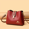 A maroon leather shoulder bag with a gold clasp and strap resting on a beige surface.