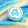 A roll of colorful gradient cake yarn is displayed on a light blue knitted fabric.