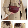 A woman models a maroon PU leather waist bag with a striped adjustable strap against a beige trench coat.
