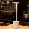 A white desk lamp with a cylindrical base and a glowing light source stands on a countertop in a kitchen setting.