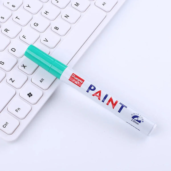 A green paint marker is placed diagonally across a white computer keyboard.