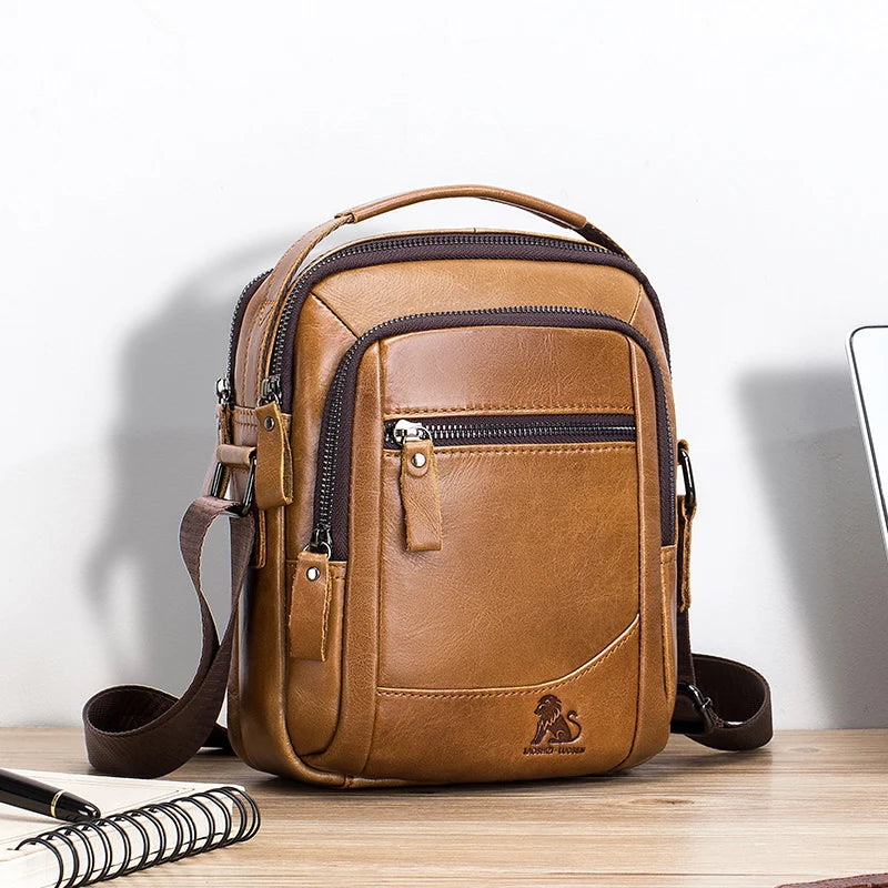 A brown men's genuine leather crossbody shoulder bag with a tan leather strap resting on a wooden surface.