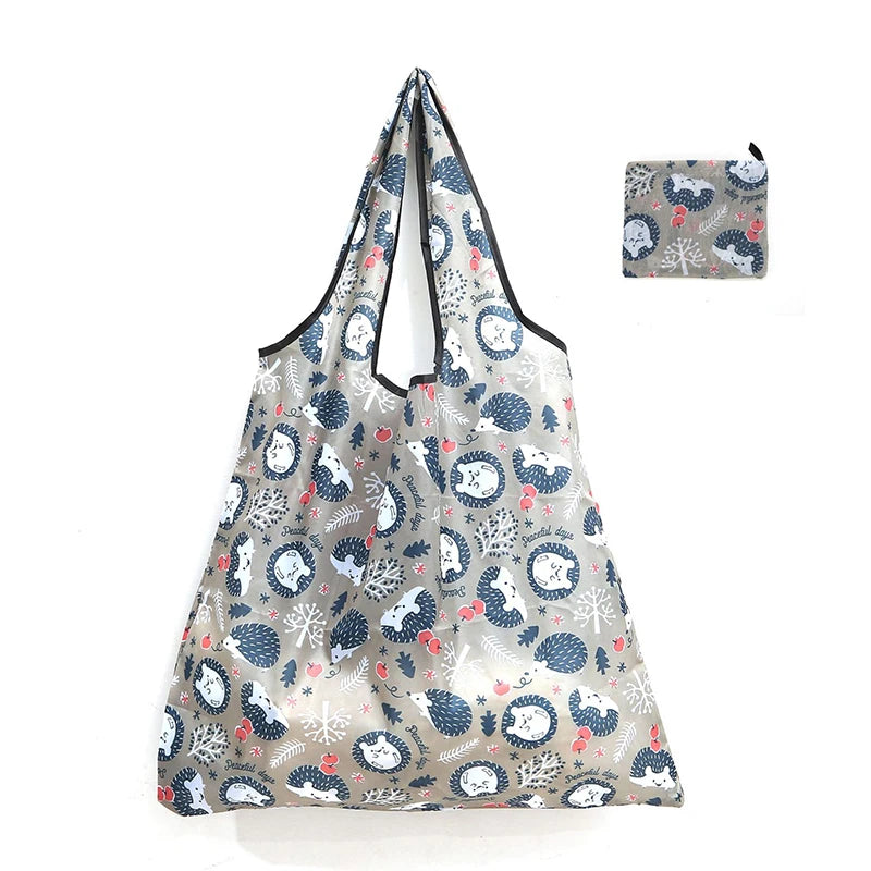 A reusable shopping tote bag featuring a gray and blue winter forest pattern, with an attached small carry pouch.