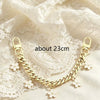 A gold chain phone strap featuring small white flower charms laid on a sheer white fabric.