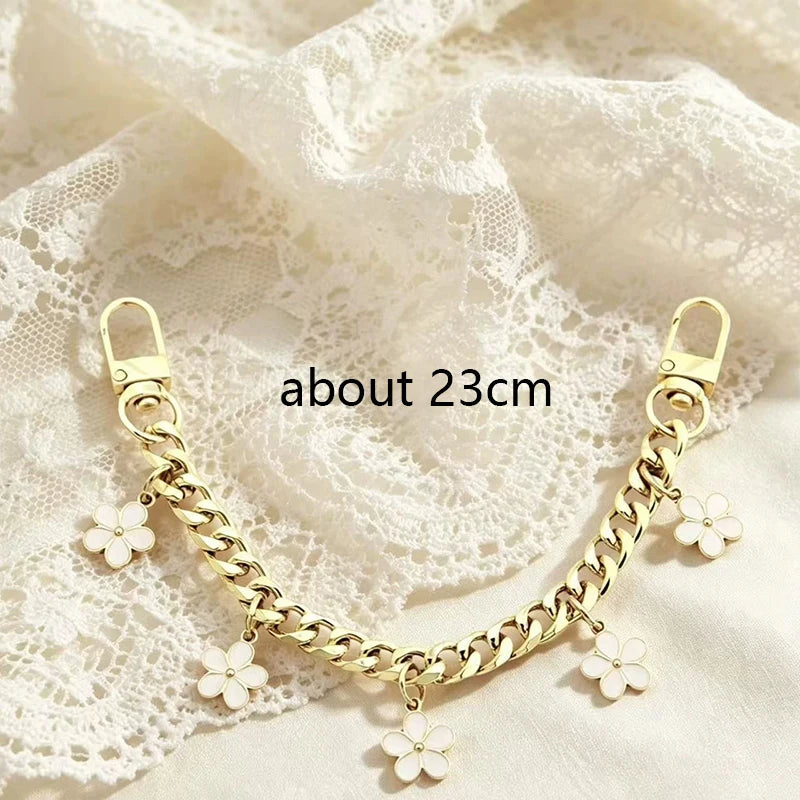 A gold chain phone strap featuring small white flower charms laid on a sheer white fabric.