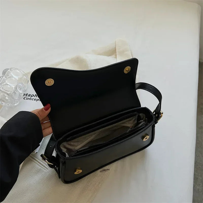 Black vintage leather crossbody bag with a flap closure resting on a white surface.
