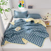 A quilted blanket with a blue and white gingham pattern is displayed on a white shelf next to pillows.
