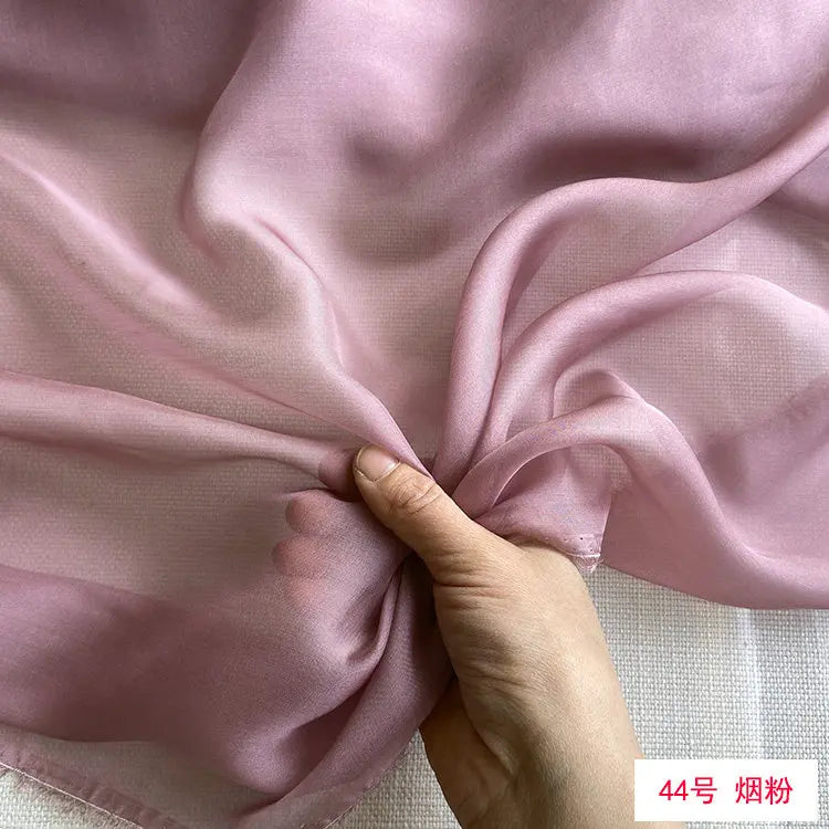 Close-up of flowing light pink mulberry silk chiffon fabric being gathered by a hand