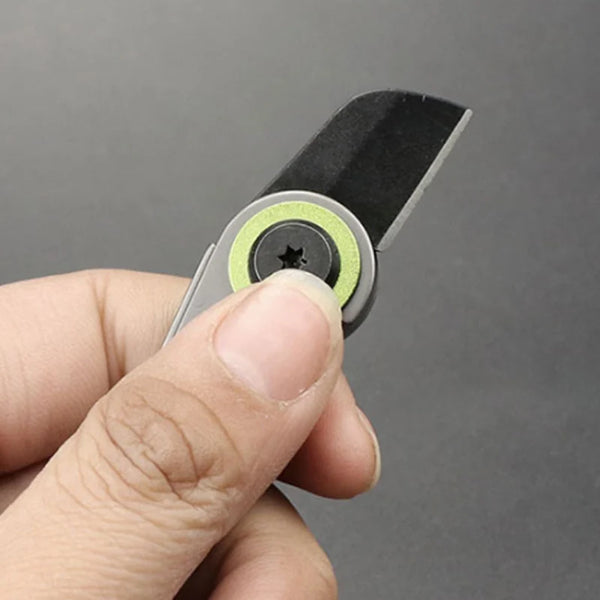 A hand holds a compact folding pocket knife with a keychain attachment, showing the blade and mechanism.