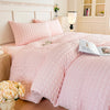 A pink lightweight seersucker duvet cover set displayed on a bed with white wooden furniture and a lamp.