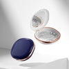 A white compact orthodontic retainer case with a hinged lid and a built-in mirror, next to a dark blue oval accessory.
