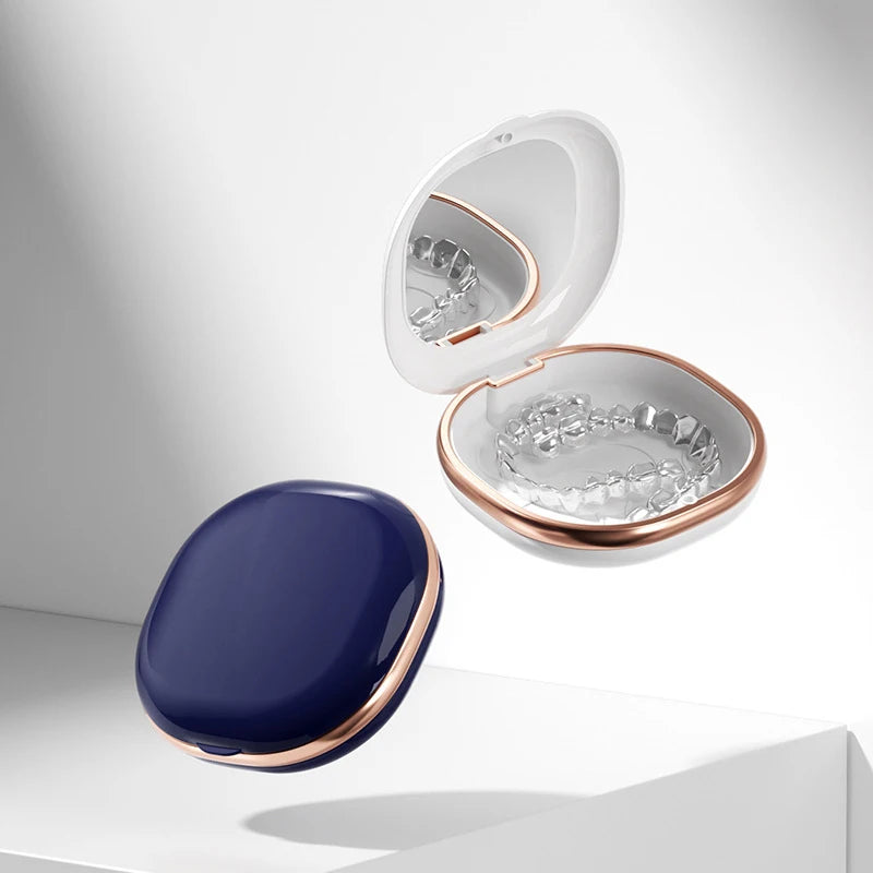 A white compact orthodontic retainer case with a hinged lid and a built-in mirror, next to a dark blue oval accessory.