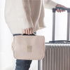 A light pink travel makeup bag with a hanging hook is held by a person next to a suitcase.