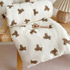 A white muslin baby blanket with brown bear pattern is rolled up and laid out on a wooden surface.