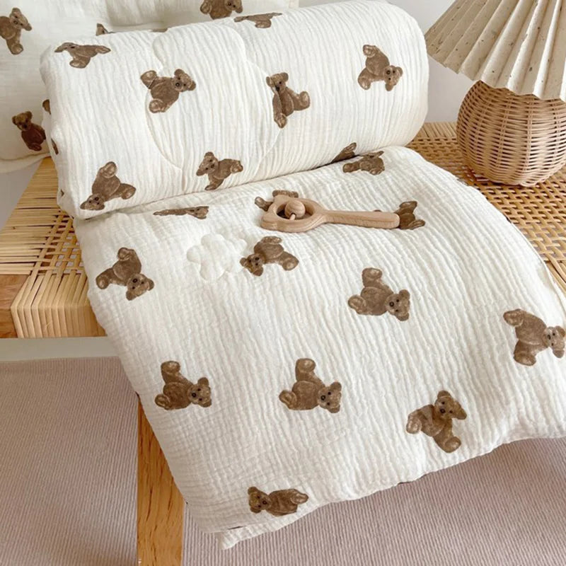 A white muslin baby blanket with brown bear pattern is rolled up and laid out on a wooden surface.