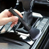 A hand is holding a black soft bristle interior detailing brush over the console of a vehicle.