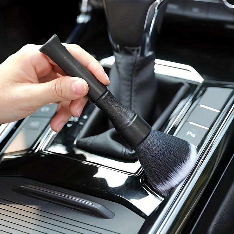 A hand is holding a black soft bristle interior detailing brush over the console of a vehicle.