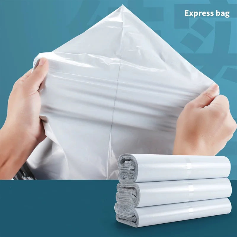 A hand is holding an open white self-sealing mailing bag, with several rolled white bags stacked below it.