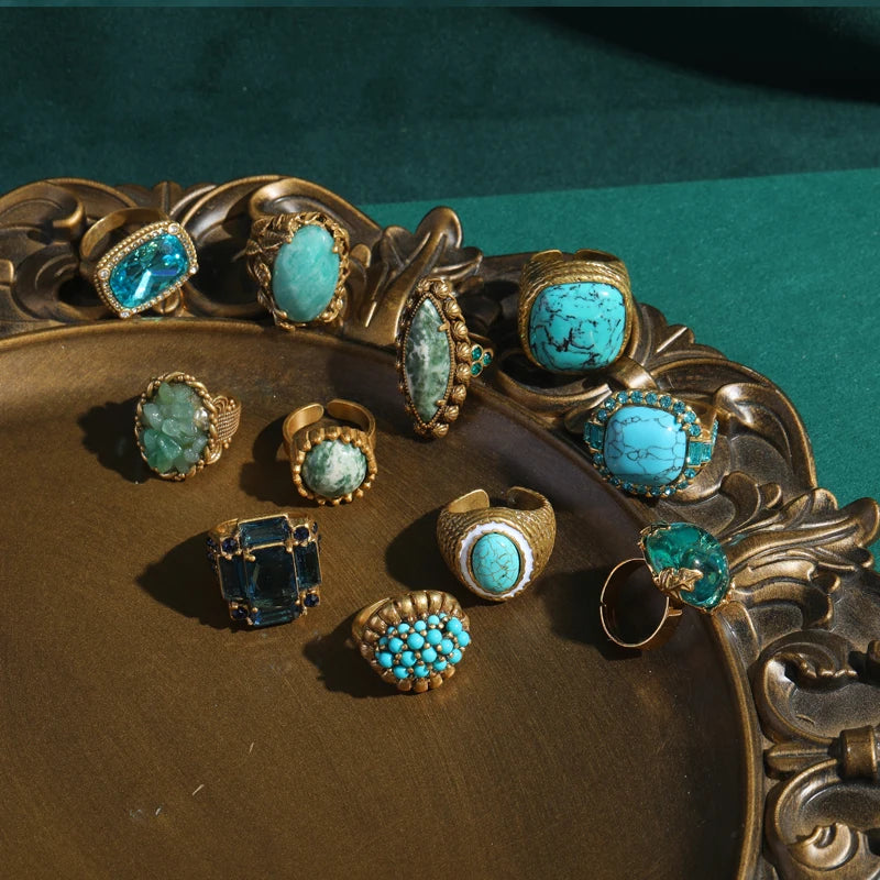 A collection of vintage sea blue crystal cocktail rings displayed on a gold-toned platter.