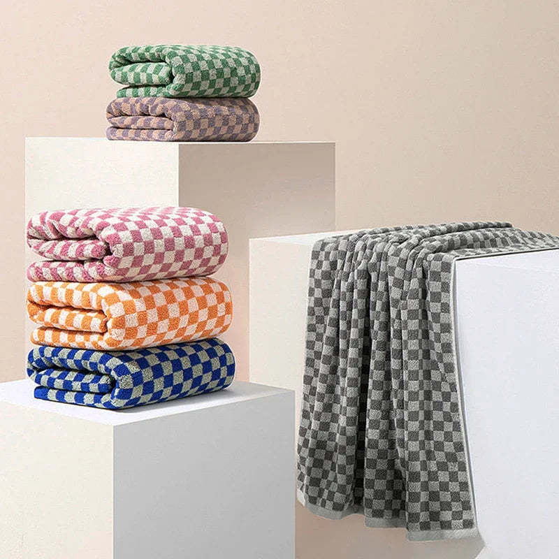 A set of three plaid cotton bath towels in shades of green, purple, and orange stacked on white display stands.