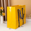 A bright yellow waterproof tote bag with black straps is shown standing upright on a white surface.