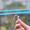 A hand holds a pink clothespin clamping a blue plastic clothesline for camping or travel.