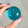 Eine Hand hält einen glatten, türgrünen Stressball vor einem hellgrauen Hintergrund.