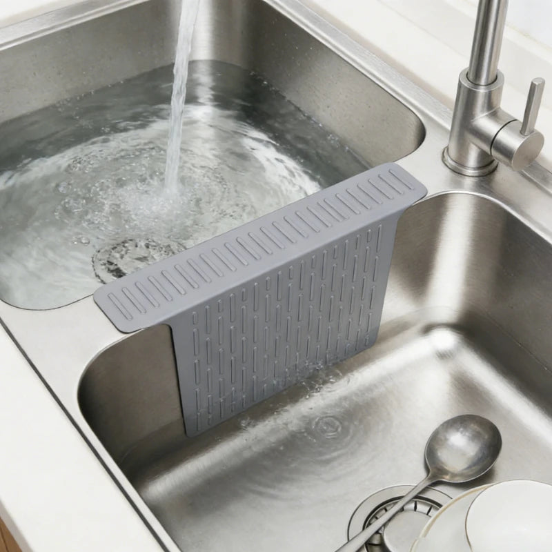 A silicone sink protector mat with drainage holes is placed in a stainless steel kitchen sink.