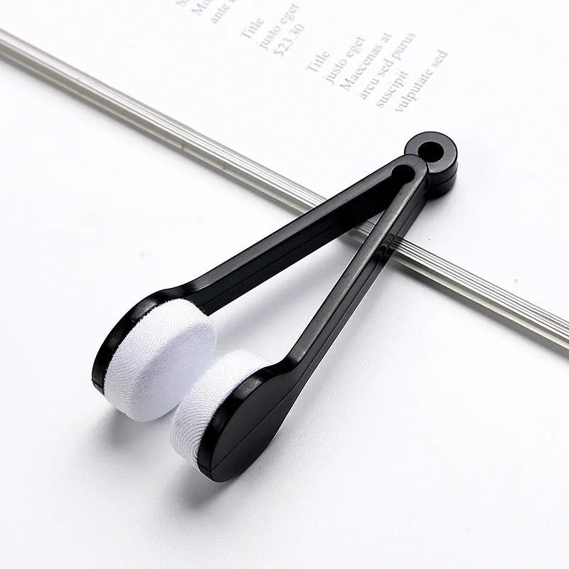 A black portable microfiber glasses cleaning cloth with a brush is shown resting on a piece of paper.