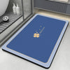 A blue non-slip bathroom mat with a gold flower design is placed on a gray tiled floor next to a shower area.