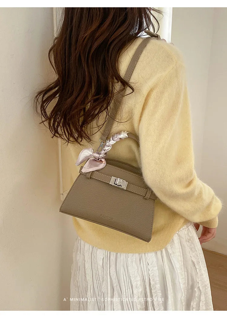 Eine Frau trägt einen gelben Pullover und hält eine elegante taupefarbene Kunstleder-Clutch.