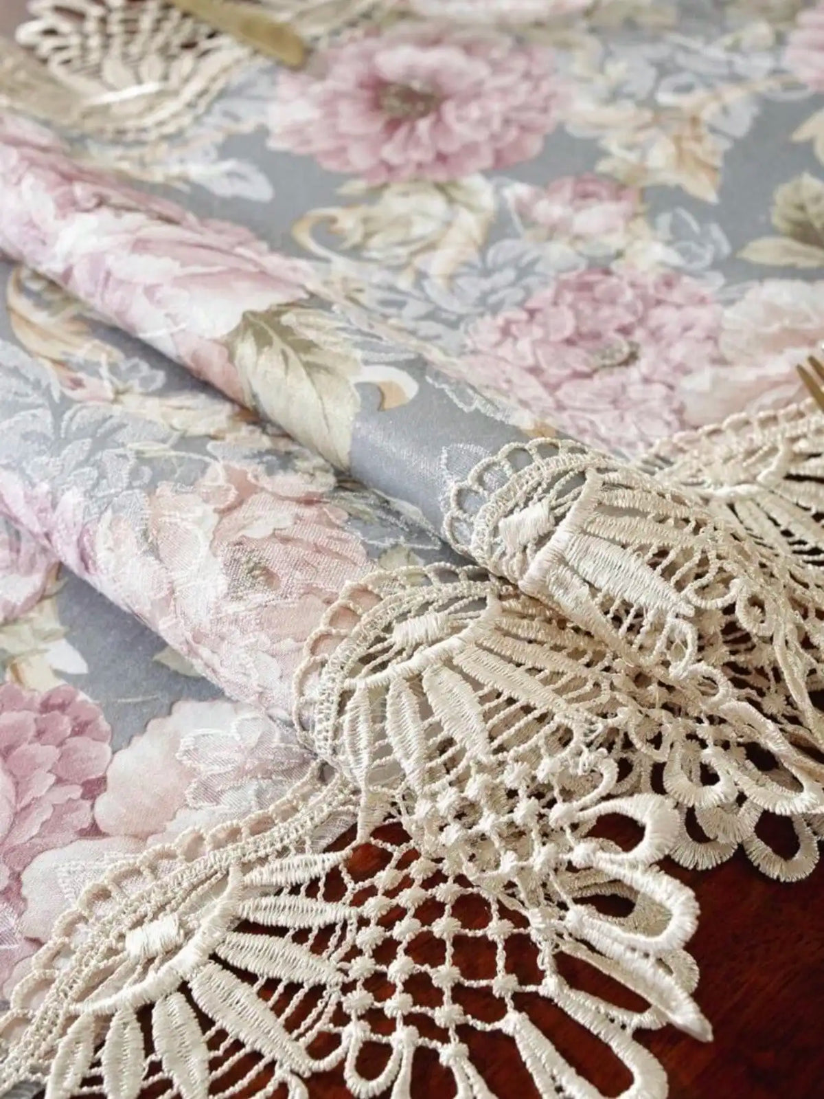 A close-up of a pink and gray floral jacquard lace table runner with delicate white embroidery.