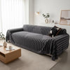 A charcoal gray bohemian striped sofa cover draped over a modern sofa in a bright living room.