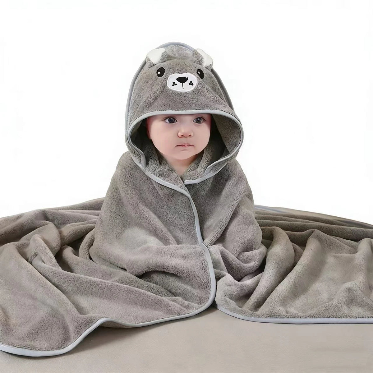 A gray hooded baby bathrobe towel with a cartoon bear face is draped on a surface.
