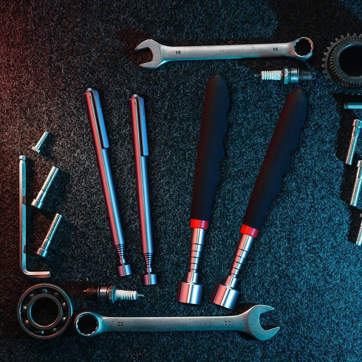 A collection of silver and black tools including a telescopic magnet pickup tool, wrenches, and various hardware components o