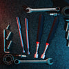 A collection of various metal tools including wrenches, pliers, and magnetic pickup tools on a dark surface.