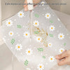 A clear, reusable EVA material mat with white daisy flowers and green leaves is being rinsed under water.