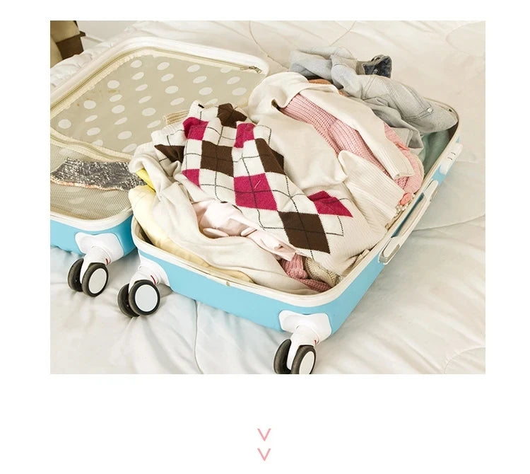 A light blue packing cube set with a lid is shown open, filled with various folded textiles and clothing on a white bed.