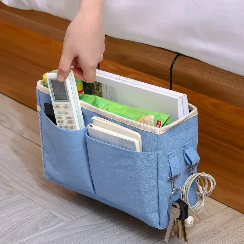 A hand is placing a white electronic device into a blue fabric storage organizer with cotton pockets.