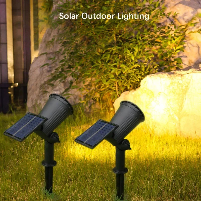 Two black solar outdoor spotlights illuminating a grassy garden area near a large rock.