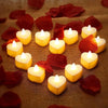 A collection of heart-shaped white LED candles resting on brown fabric surrounded by red rose petals.