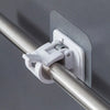 A white adhesive curtain rod hook clamp is mounted on a silver metal rod against a gray wall.