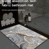 A rectangular bathroom mat with a marbled gray and gold pattern is displayed on a dark surface.