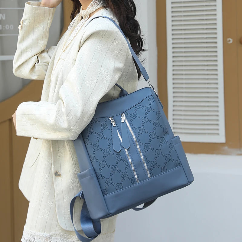 A woman holds a blue leather anti-theft backpack against a light-colored coat.