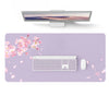 A silver laptop is displayed above a purple desk pad featuring pink cherry blossoms and a white wireless mouse.