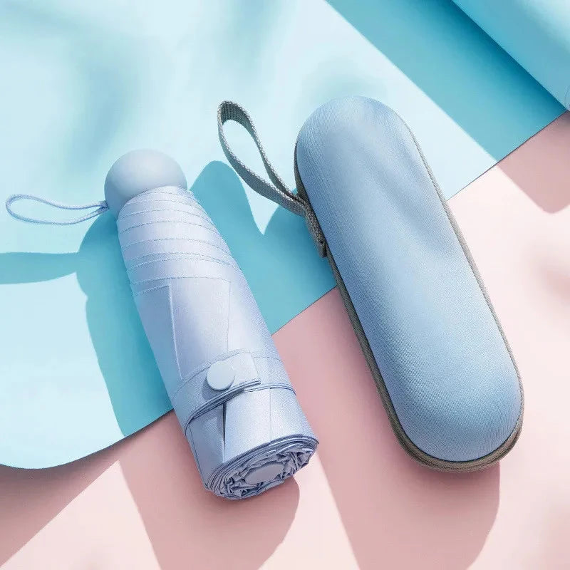 Light blue compact 5-fold travel umbrella with a fabric sleeve resting on a pink surface.