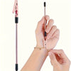 A hand is using a pink retractable bracelet fastening tool to secure a gold-colored bracelet on a wrist.
